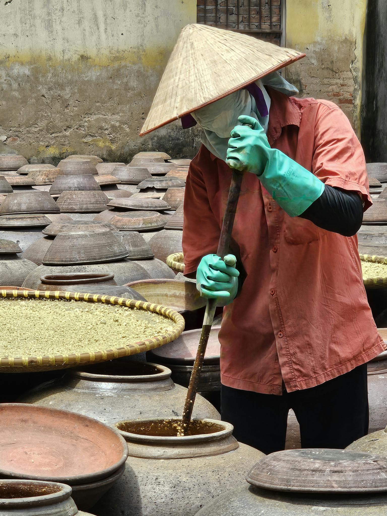 A worker stirs fermentation jars in a Vietnamese courtyard, showcasing traditional food production.