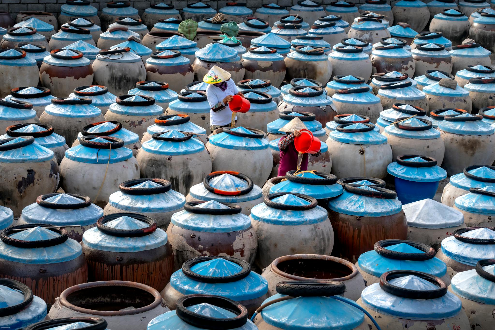 Aerial view of traditional fermentation pots with workers in Asian market setting.